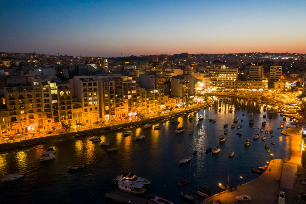 A stunning cityscape of Sliema, Malta at twilight, featuring illuminated buildings along the waterfront.