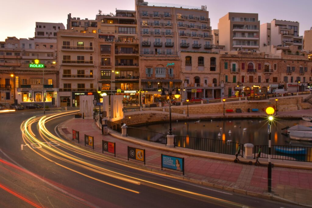 Long exposure photo of Saint Julian's Bay in Malta at sunset, showcasing vibrant city lights and architecture.